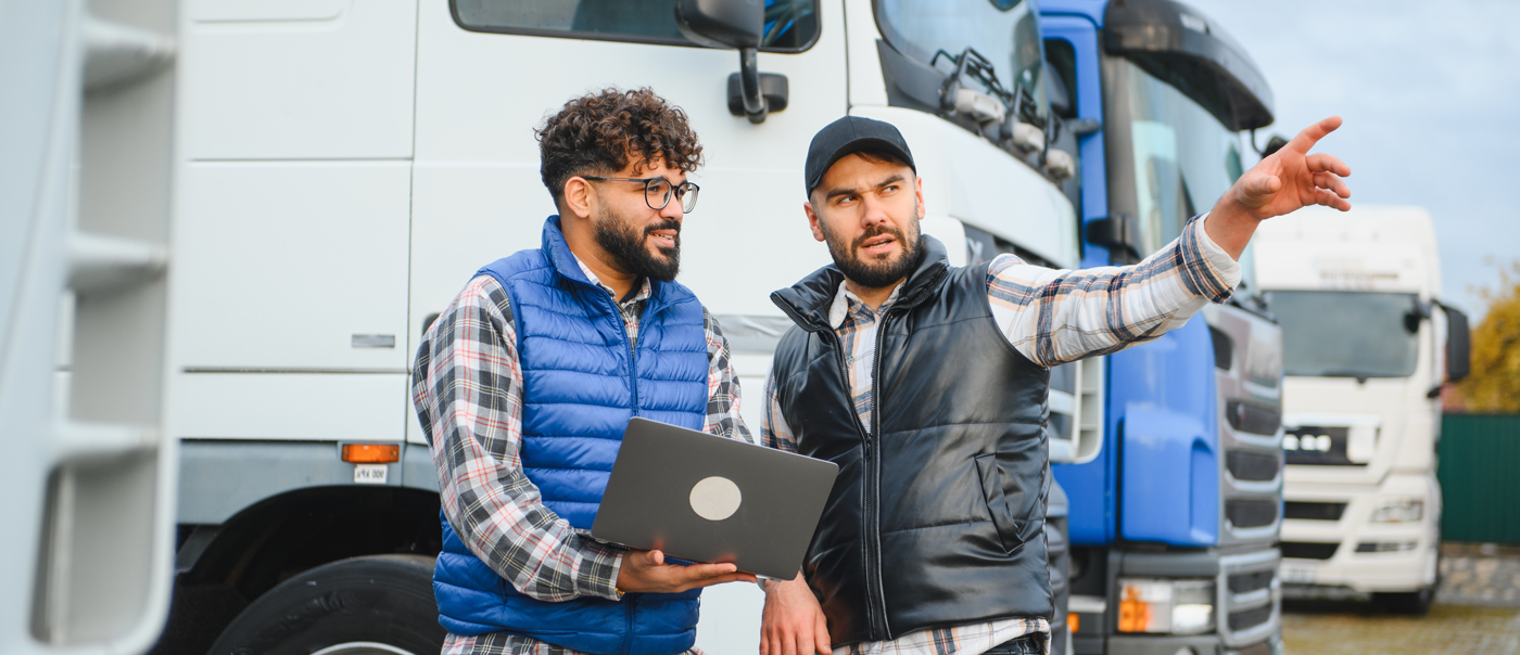 two men discussing business in front of a fleet of trucks and trailers